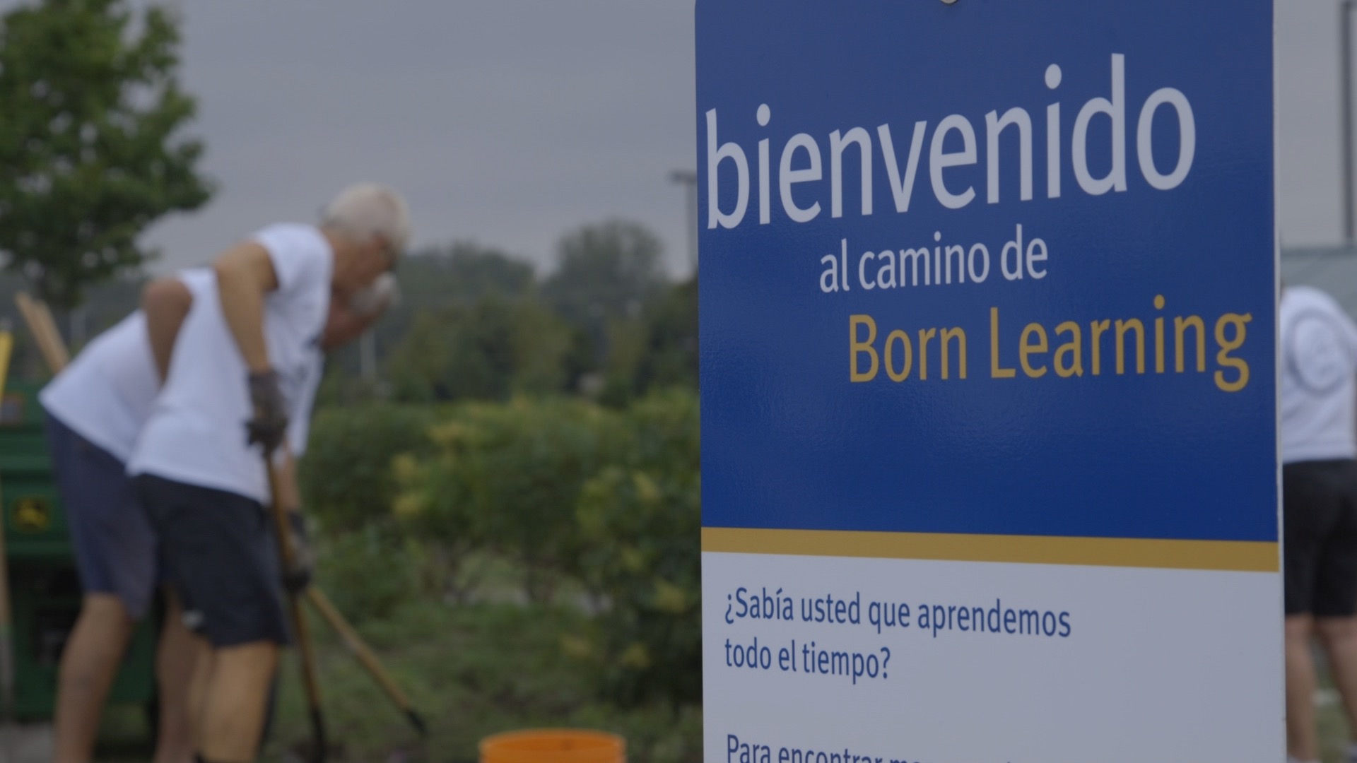 Bienvendido al camino de Born Learning Trail. You will also see two men raking in the background.